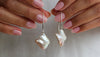 Pearl earrings held between two hands with a neutral background