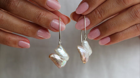 Pearl earrings held between two hands with a neutral background